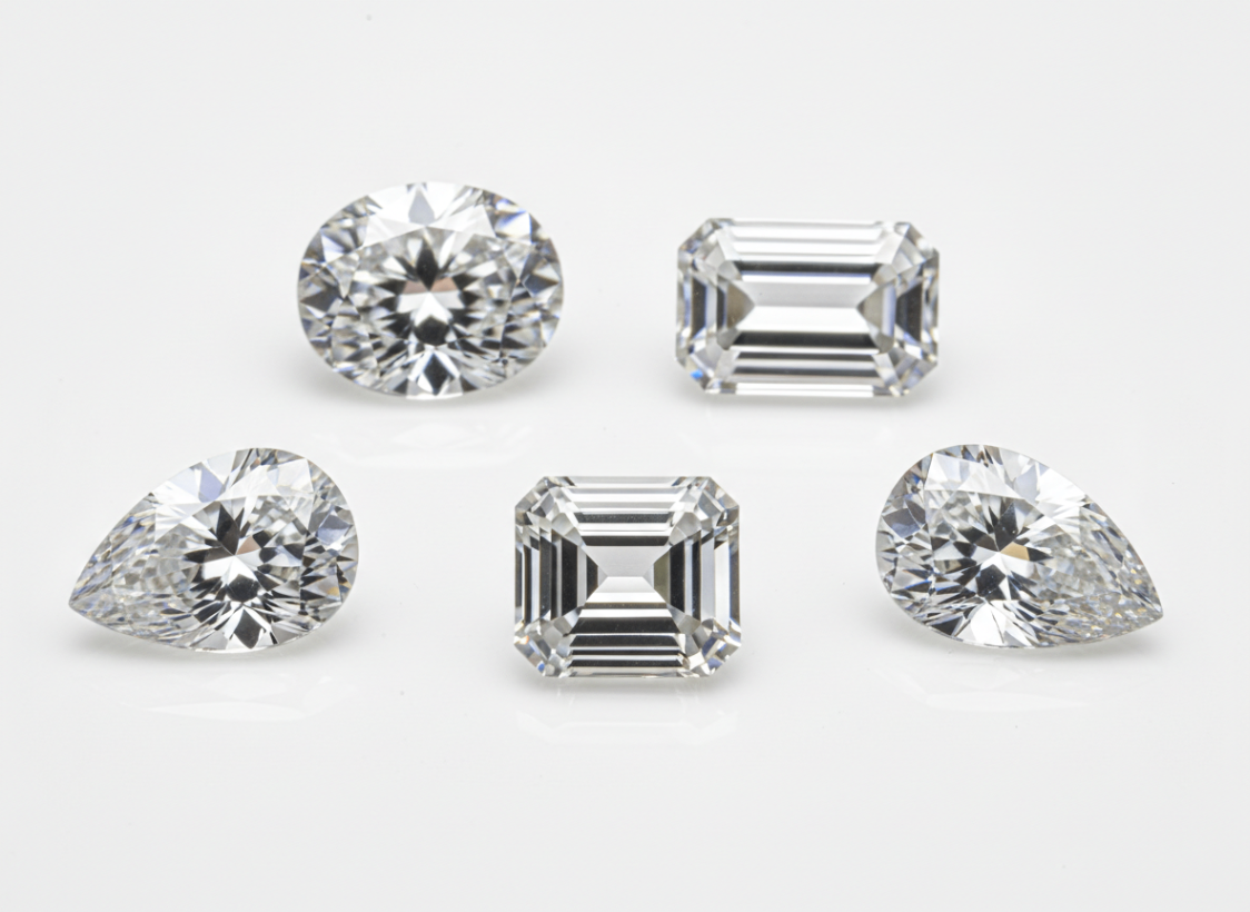 Moissanite gemstones in round, emerald, and pear cuts photographed on a light background